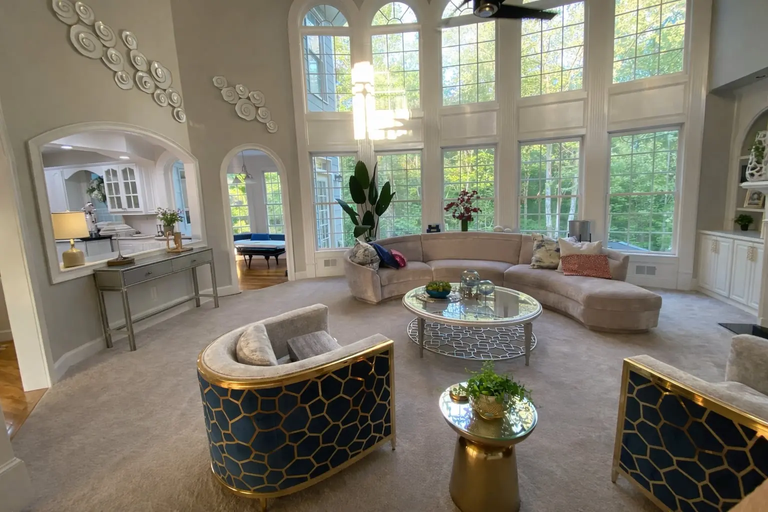 Luxury sitting room with navy and gold geometric accent chairs, curved sectional sofa, and floor to ceiling windows in a Hoschton Georgia home designed by Welcome Home Interiors