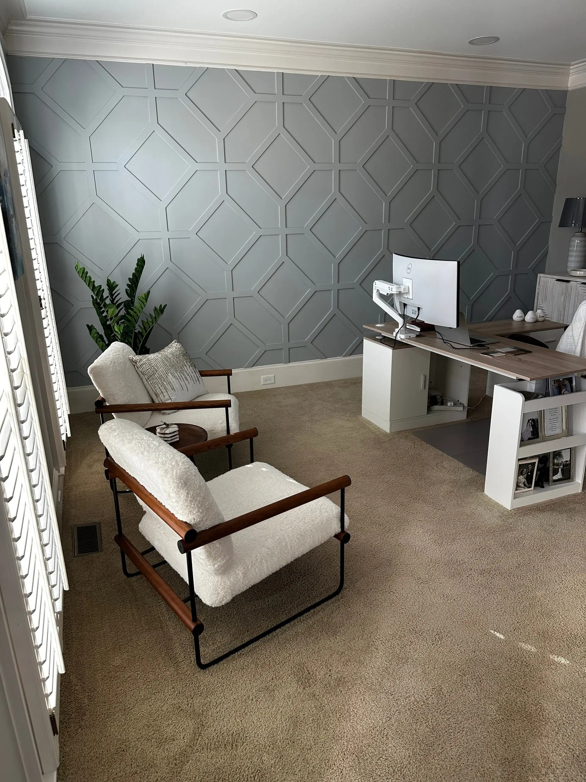 Home office with a gray geometric-paneled wall, two white bouclé armchairs and a white desk with a monitor
